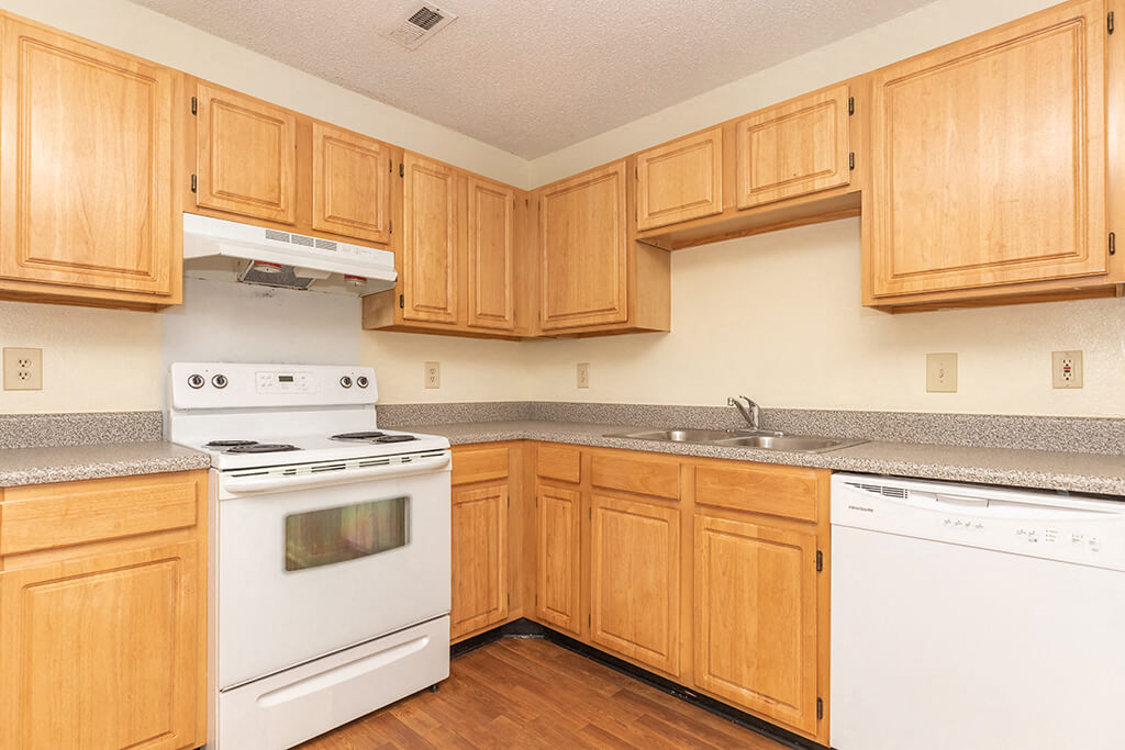 A kitchen with white appliances and wooden cabinets at the Greens of Pine Glen Apartments in Durham, North Carolina.